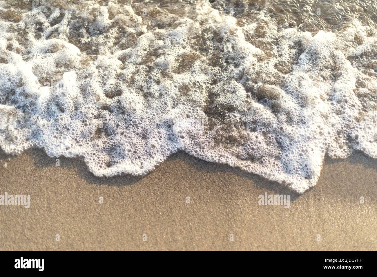 Gros plan des vagues qui frappent la plage en créant des bulles. Banque D'Images