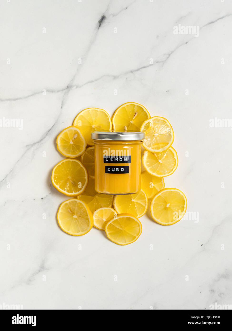 Délicieux citron-lait fait maison. Bocal en verre au citron curd sur des tranches de citron sur fond de marbre blanc. Vue de dessus ou plan de travail. Verticale. Étiquette adhésive noire avec texte citron sur le pot Banque D'Images