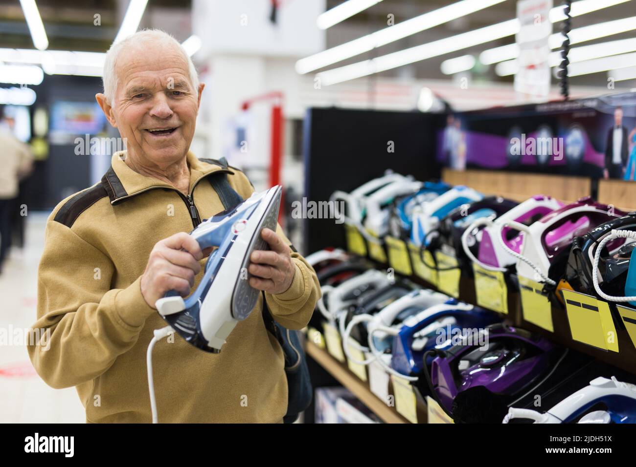 homme âgé qui choisit le fer dans la salle d'exposition du magasin d'appareils électriques Banque D'Images