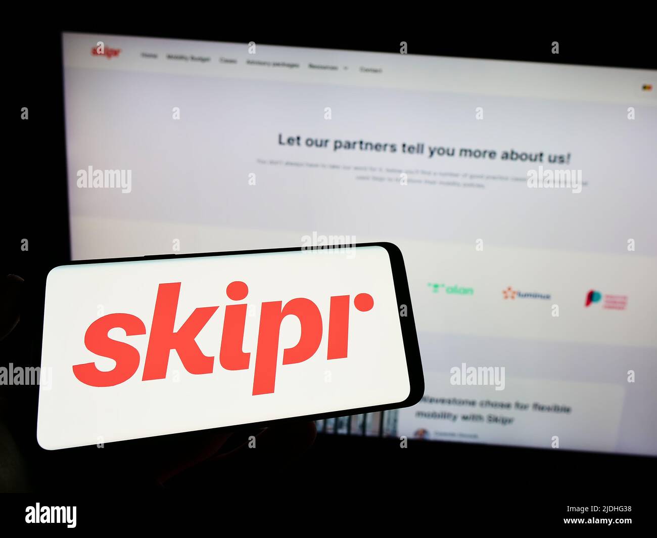 Personne tenant un smartphone avec le logo de la société belge de mobilité Skipr sa à l'écran devant le site Web. Mise au point sur l'affichage du téléphone. Banque D'Images