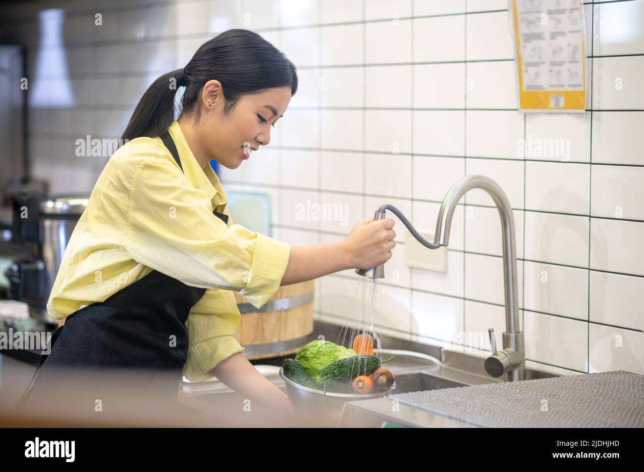 Femme debout sur le côté de l'appareil photo laver les légumes dans un bol Banque D'Images