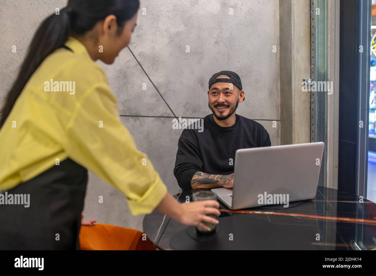 Homme assis à un ordinateur portable et serveur de femme debout Banque D'Images