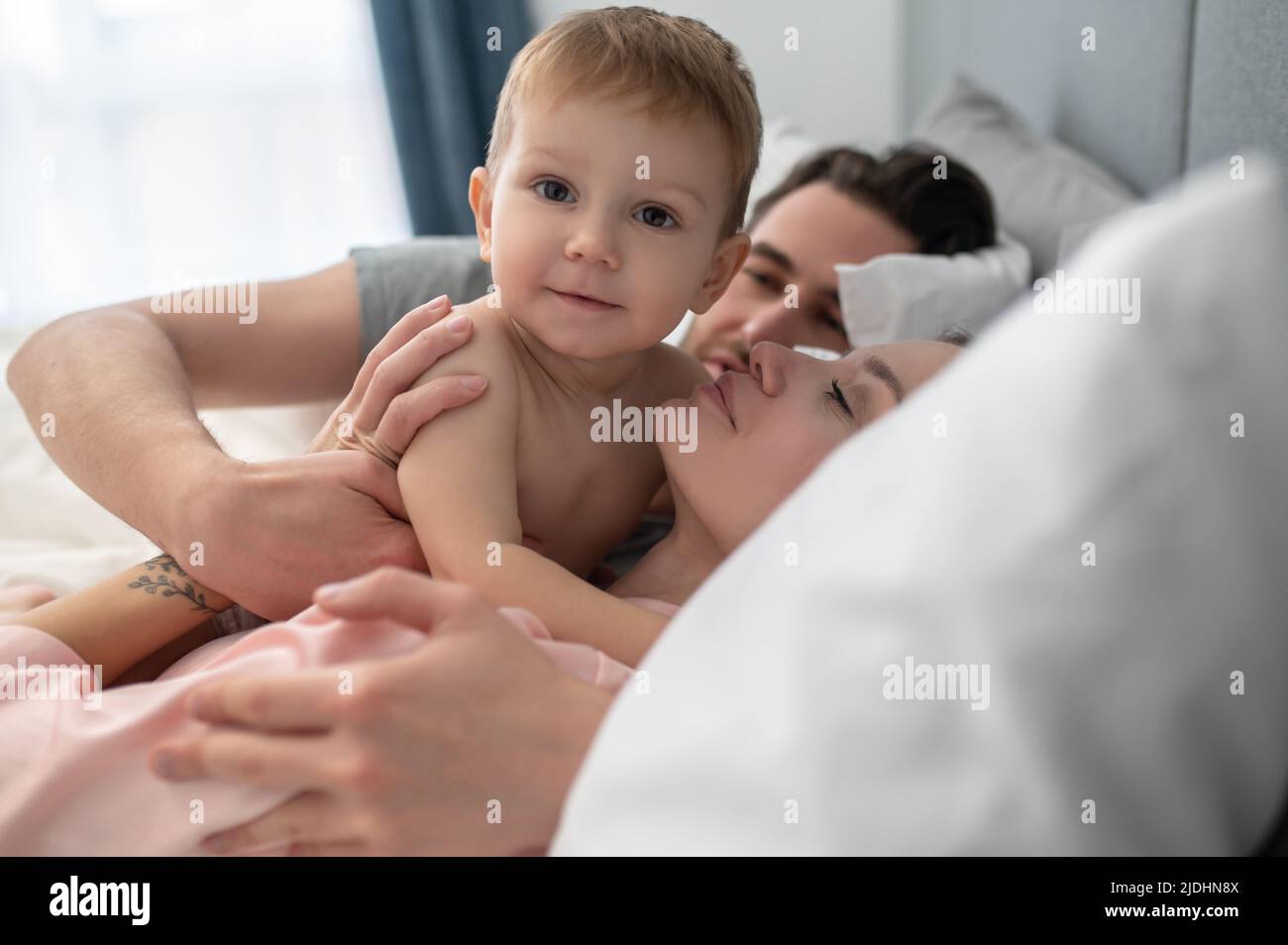 Parents qui embrasent un petit enfant regardant l'appareil photo Banque D'Images