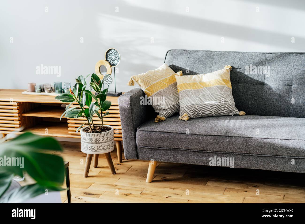 Intérieur élégant du salon avec console design, décor, canapé gris avec oreillers graphiques. Murs blancs, plantes vertes dans les pots. Bois clair Banque D'Images Intérieur élégant du salon avec console design, décor, canapé gris avec oreillers graphiques. Murs blancs, plantes vertes dans les pots. Bois clair Banque D'Images