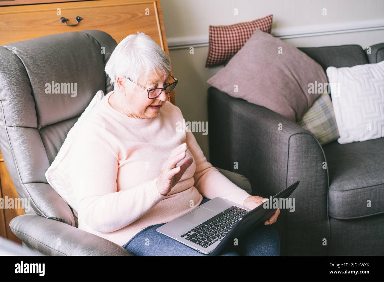Grand-mère senior assise sur un fauteuil, regardant l'écran d'un ordinateur portable. Femme mûre aux cheveux gris lisant des nouvelles, discutant avec la famille, regardant la vidéo, en ligne Banque D'Images Grand-mère senior assise sur un fauteuil, regardant l'écran d'un ordinateur portable. Femme mûre aux cheveux gris lisant des nouvelles, discutant avec la famille, regardant la vidéo, en ligne Banque D'Images