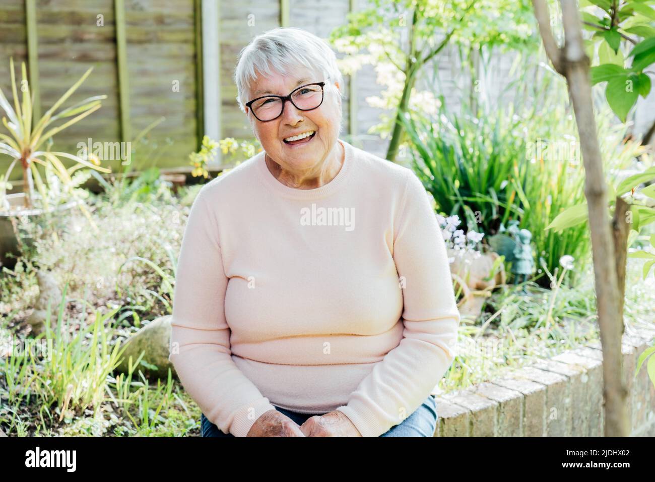 Portrait d'une grand-mère à la retraite, mûre et souriante, en lunettes. Heureuse femme âgée souriante assise dans son jardin verdoyant et profitant de sa retraite Banque D'Images Portrait d'une grand-mère à la retraite, mûre et souriante, en lunettes. Heureuse femme âgée souriante assise dans son jardin verdoyant et profitant de sa retraite Banque D'Images