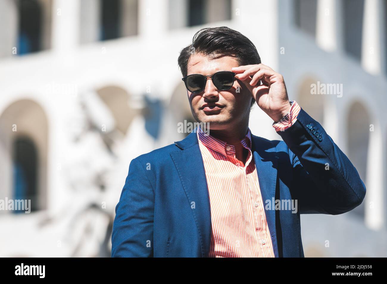 Homme d'affaires avec lunettes de soleil. Veste et chemise bleu. En arrière-plan un bâtiment. Banque D'Images