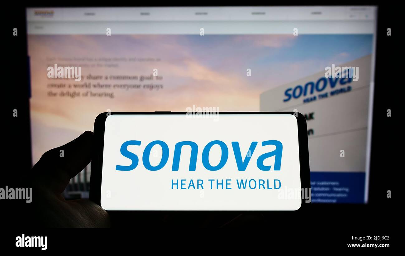 Personne tenant un smartphone avec le logo de la société suisse de soins auditifs Sonova Holding AG à l'écran devant le site Web. Mise au point sur l'affichage du téléphone. Banque D'Images
