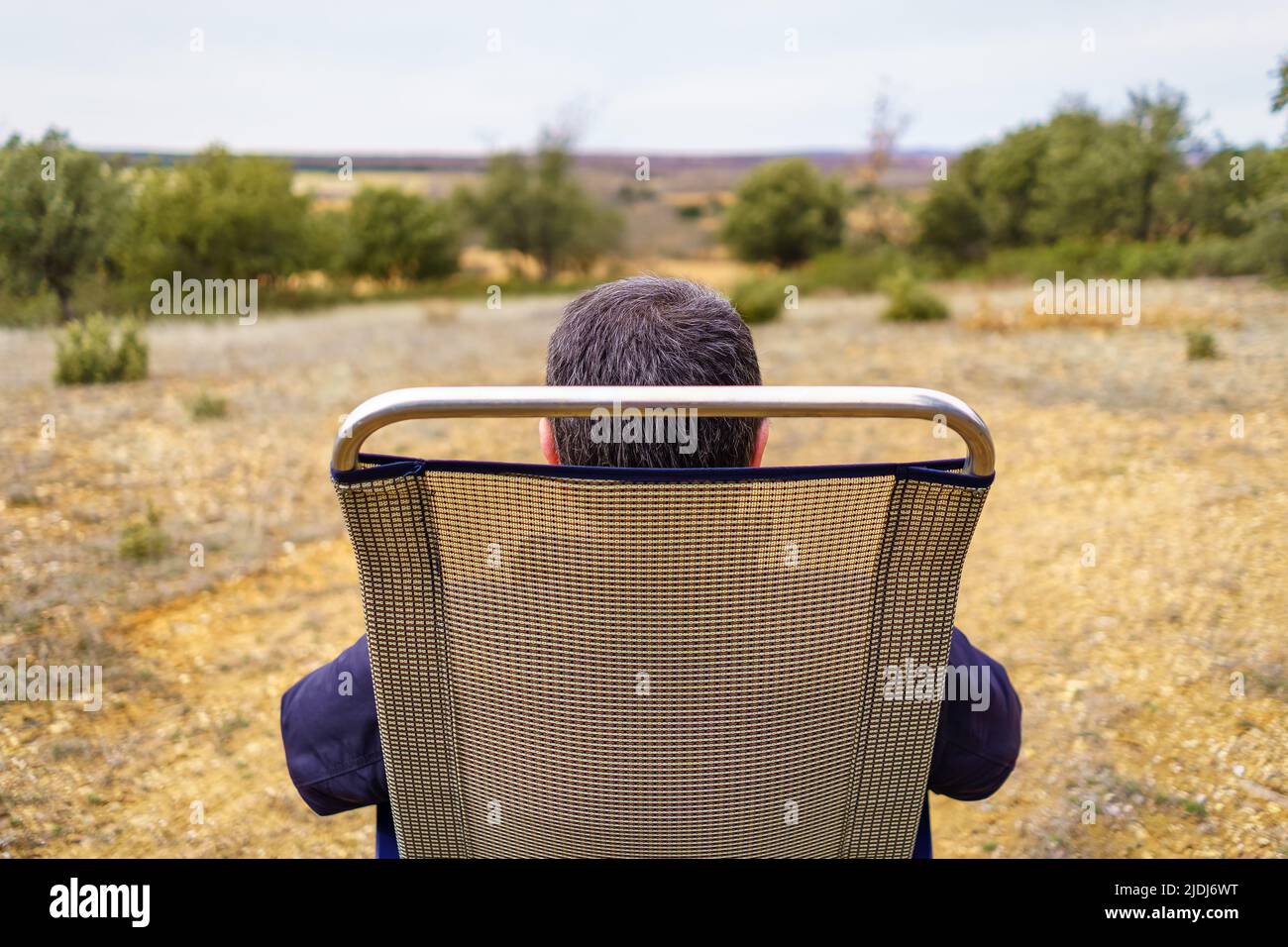 Homme de l'arrière assis dans une chaise de camping, appréciant la campagne. Banque D'Images