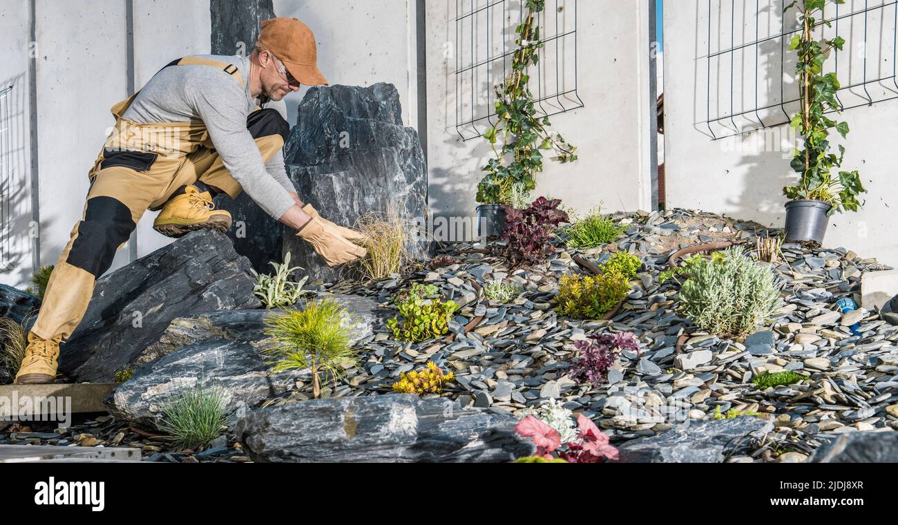 Caucasien professionnel paysagiste jardinier dans sa finition 40s Nouveau jardin résidentiel plantation de petites plantes à côté de la clôture moderne en béton Banque D'Images