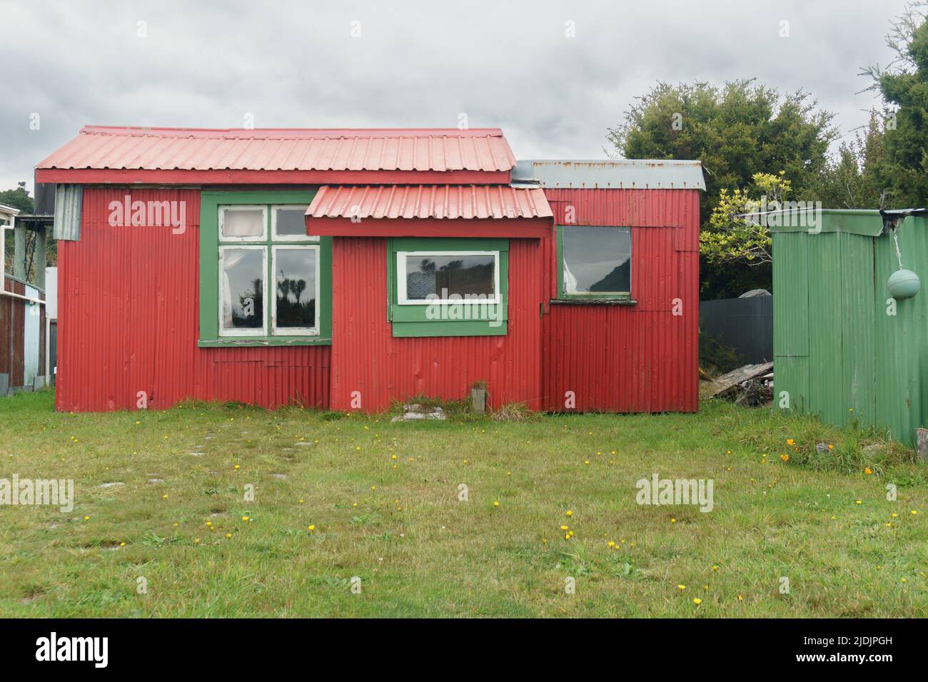 Maison ou lot de vacances rouge et vert vif dans une ville côtière de Nouvelle-Zélande éloignée. Banque D'Images