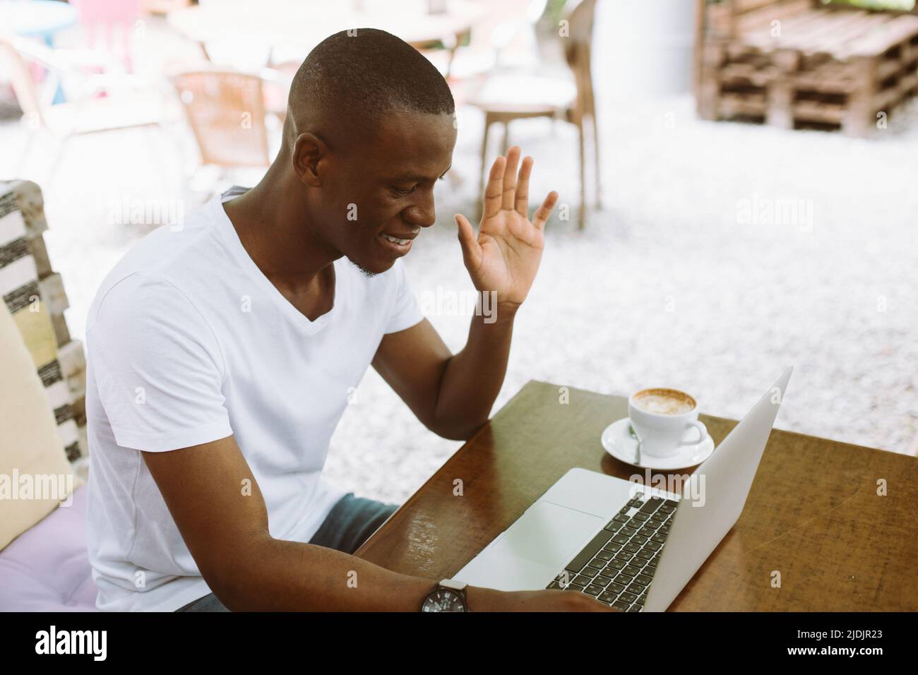 Homme d'affaires souriant et détendu avec ordinateur portable, levant la main, saluant, regarde le moniteur. Bureau indépendant en ligne Banque D'Images