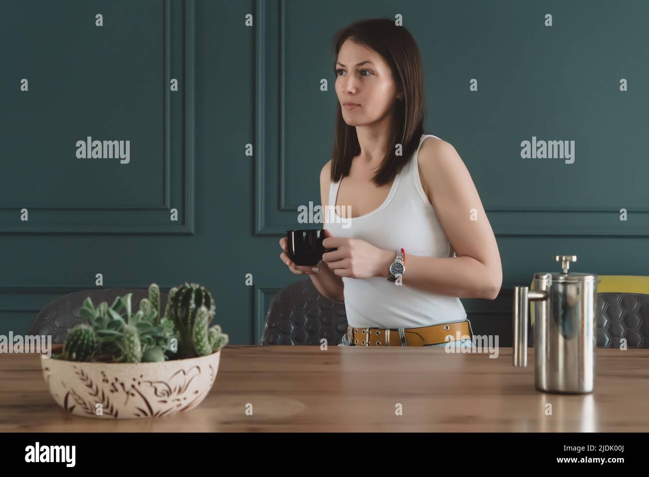 Jeune femme de brunette réfléchie et belle buvant du thé dans la cuisine seule à la maison. Banque D'Images