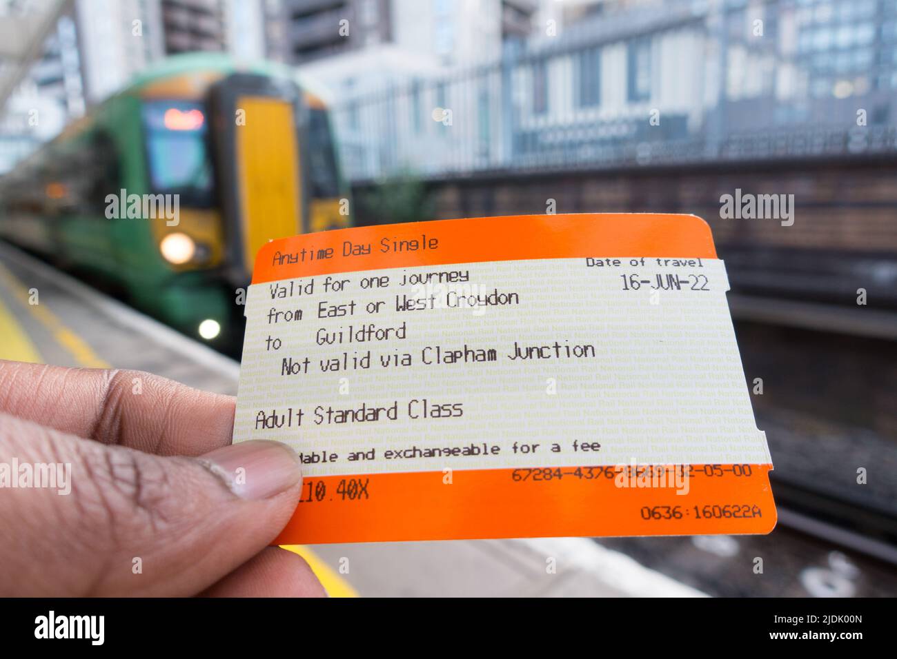 Main d'homme adulte tenant un billet de train britannique avec train en arrière-plan Banque D'Images
