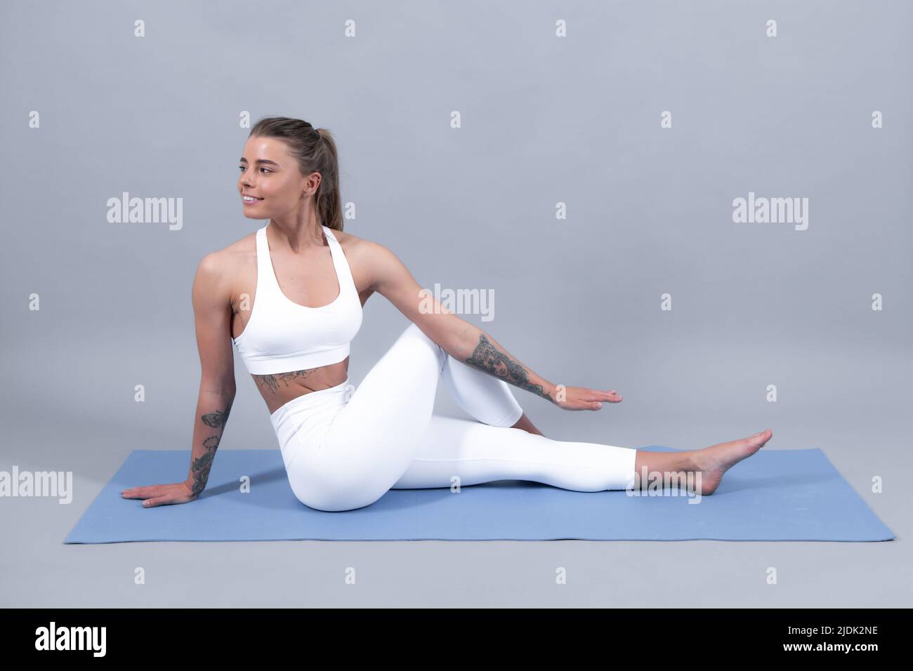 Femme de fitness. Belle jeune fille dans les vêtements de sport faisant des étirements pour les jambes. Vêtements de sport, vêtements de sport. Jeune beau modèle sur l'entraînement près de gris Banque D'Images