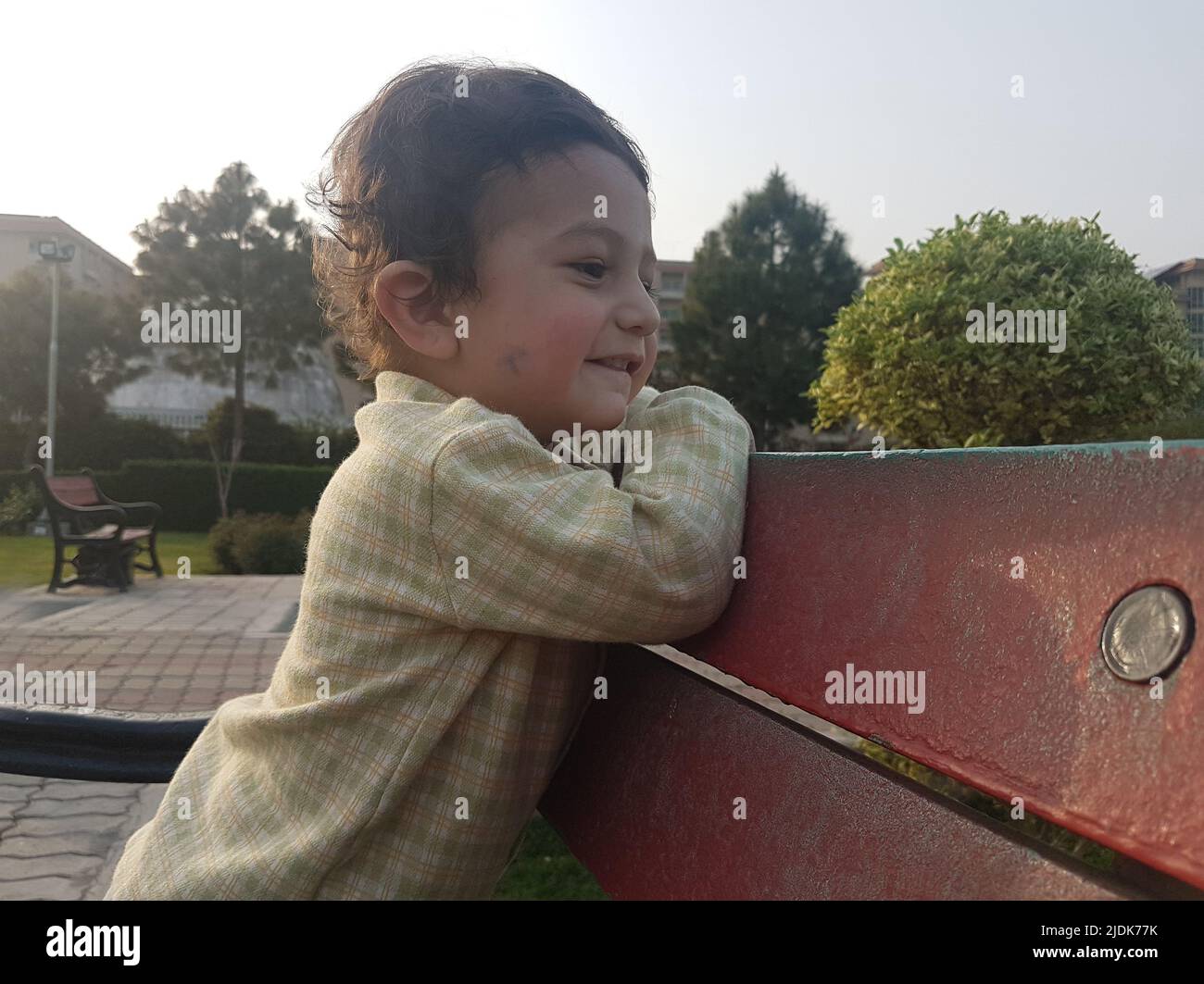 Petit garçon mignon debout sur un banc dans un parc. Banque D'Images