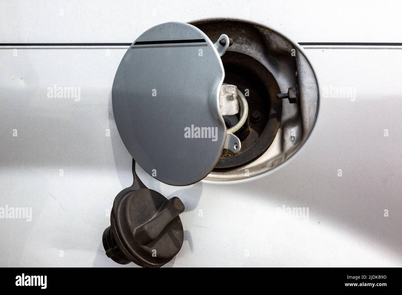 Un bouchon à essence est suspendu à une trappe de remplissage de carburant ouverte sur une voiture blanche. Banque D'Images
