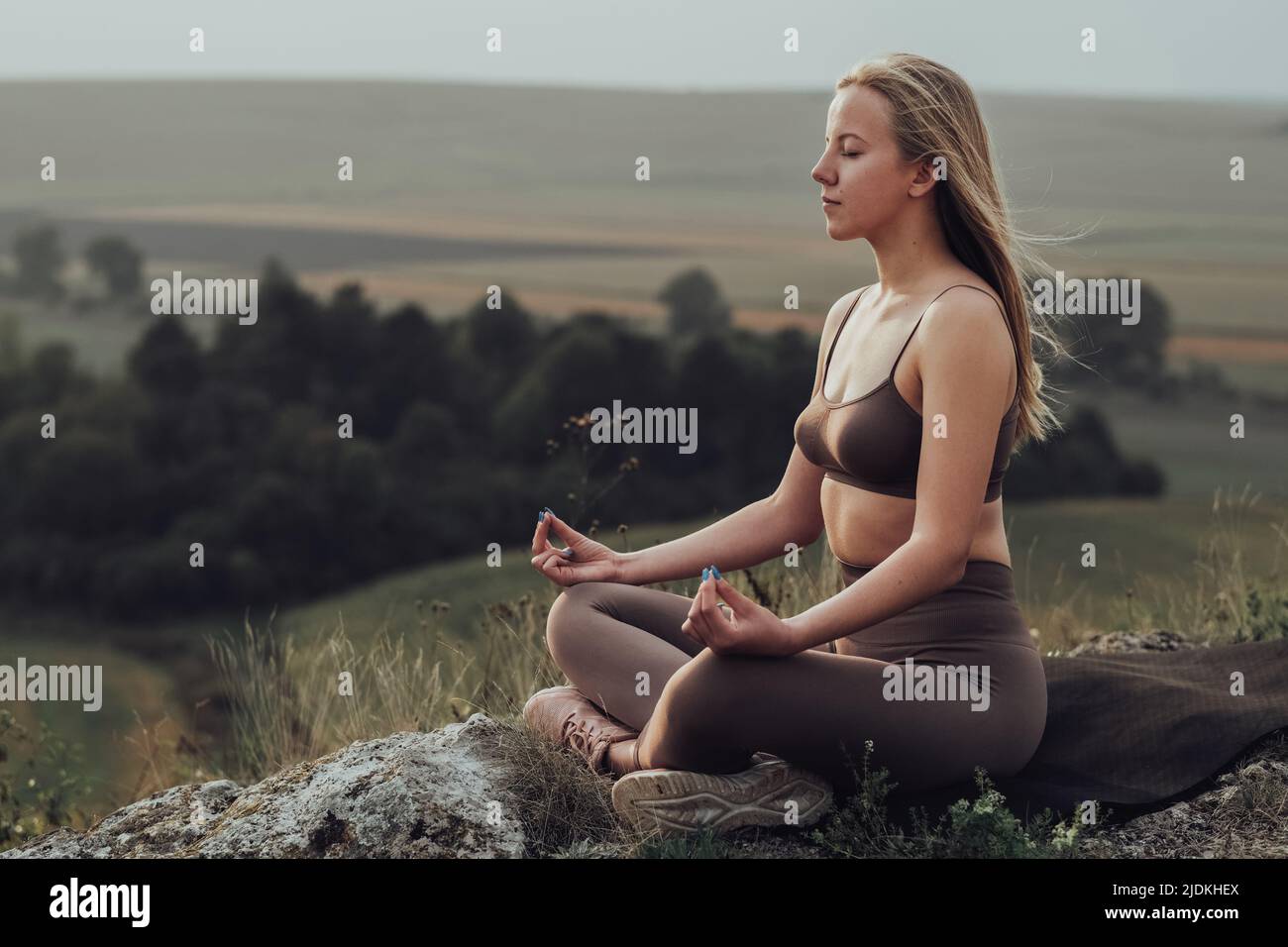 Fille sportive assise dans la posture du Lotus et faisant des exercices de méditation sur le dessus d'une colline, la jeune femme pratique le yoga à l'extérieur avec paysage panoramique à Banque D'Images