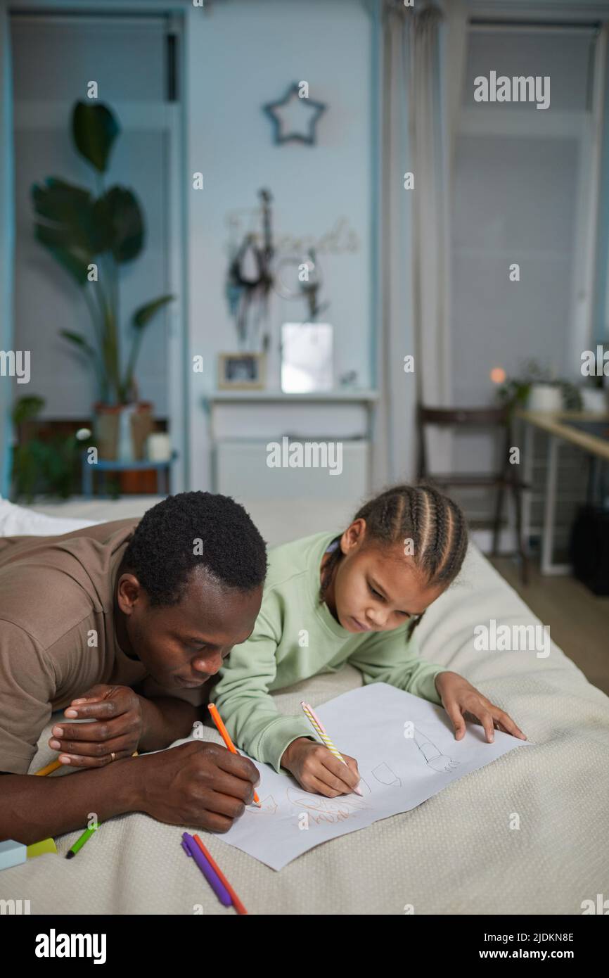 Portrait vertical d'un père noir aimant avec la fille qui se dessine ensemble tout en étant allongé sur le lit à la maison, espace de copie Banque D'Images