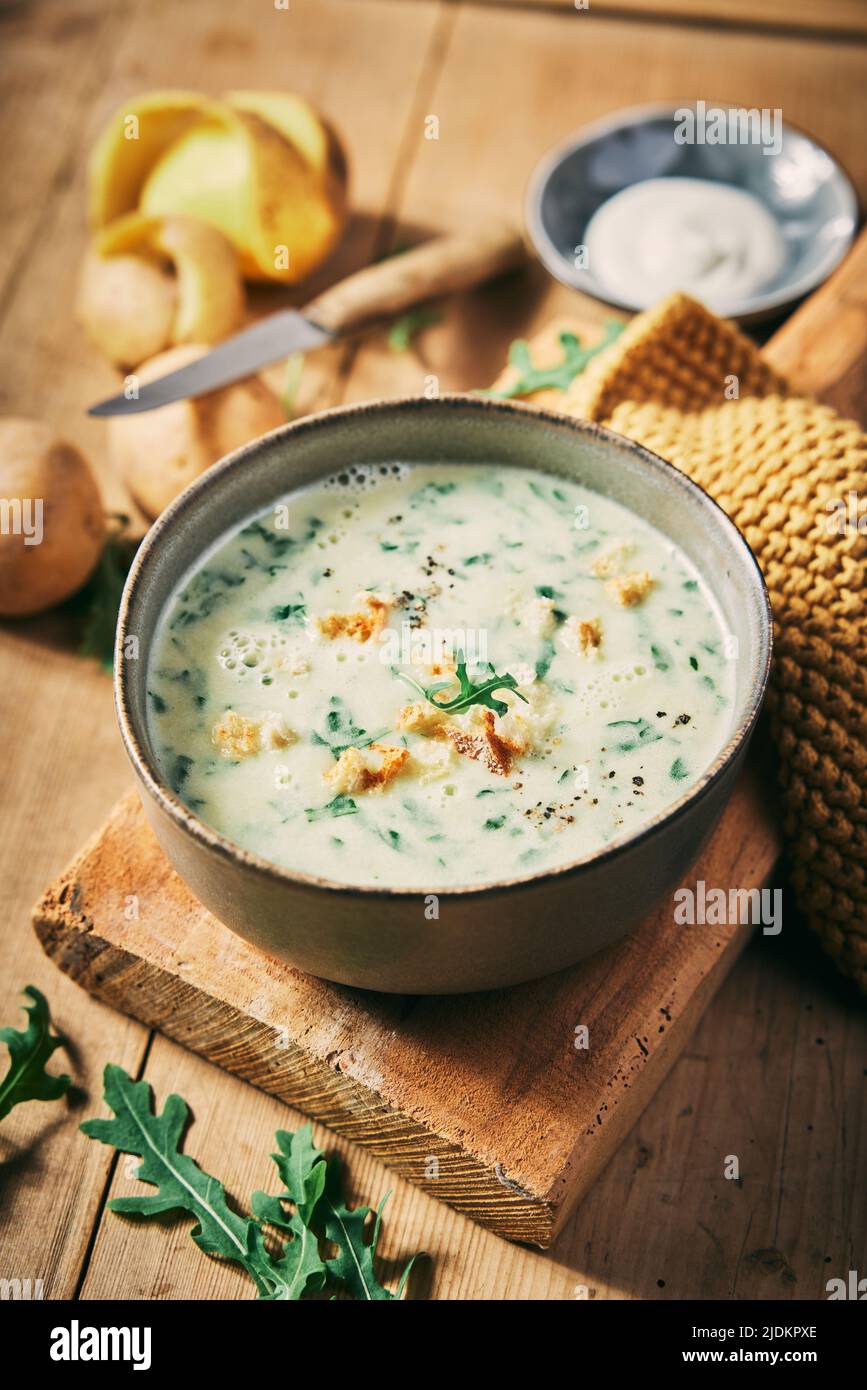 Une délicieuse soupe de rucola à la crème servie sur une table en bois avec des pommes de terre pelées et de la crème aigre dans une cuisine légère Banque D'Images