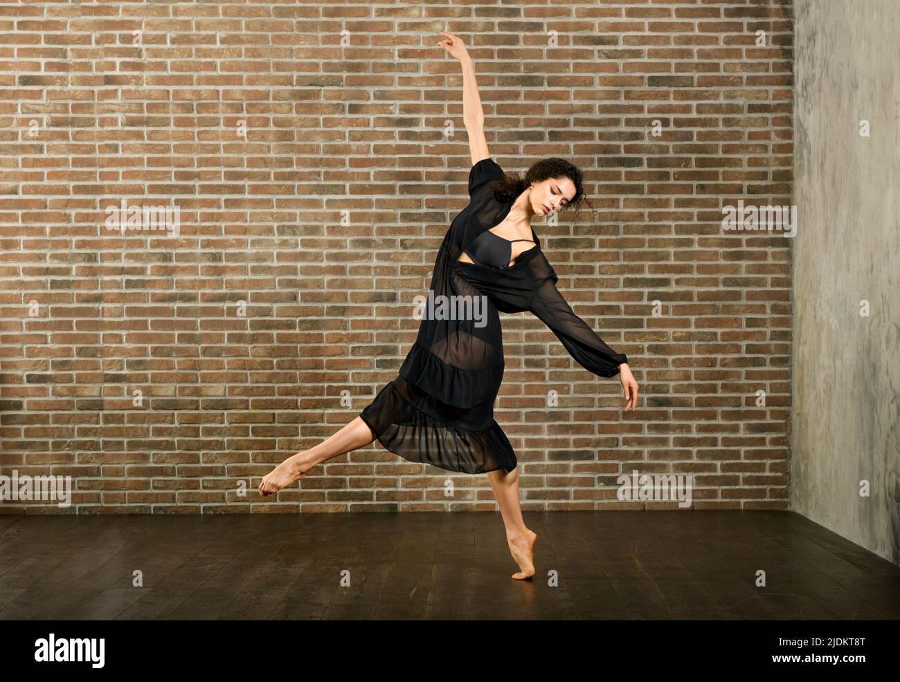 Un corps complet de danseuse de ballet pieds nus flexible debout sur une jambe tout en répétant la danse contre le mur de briques en studio Banque D'Images