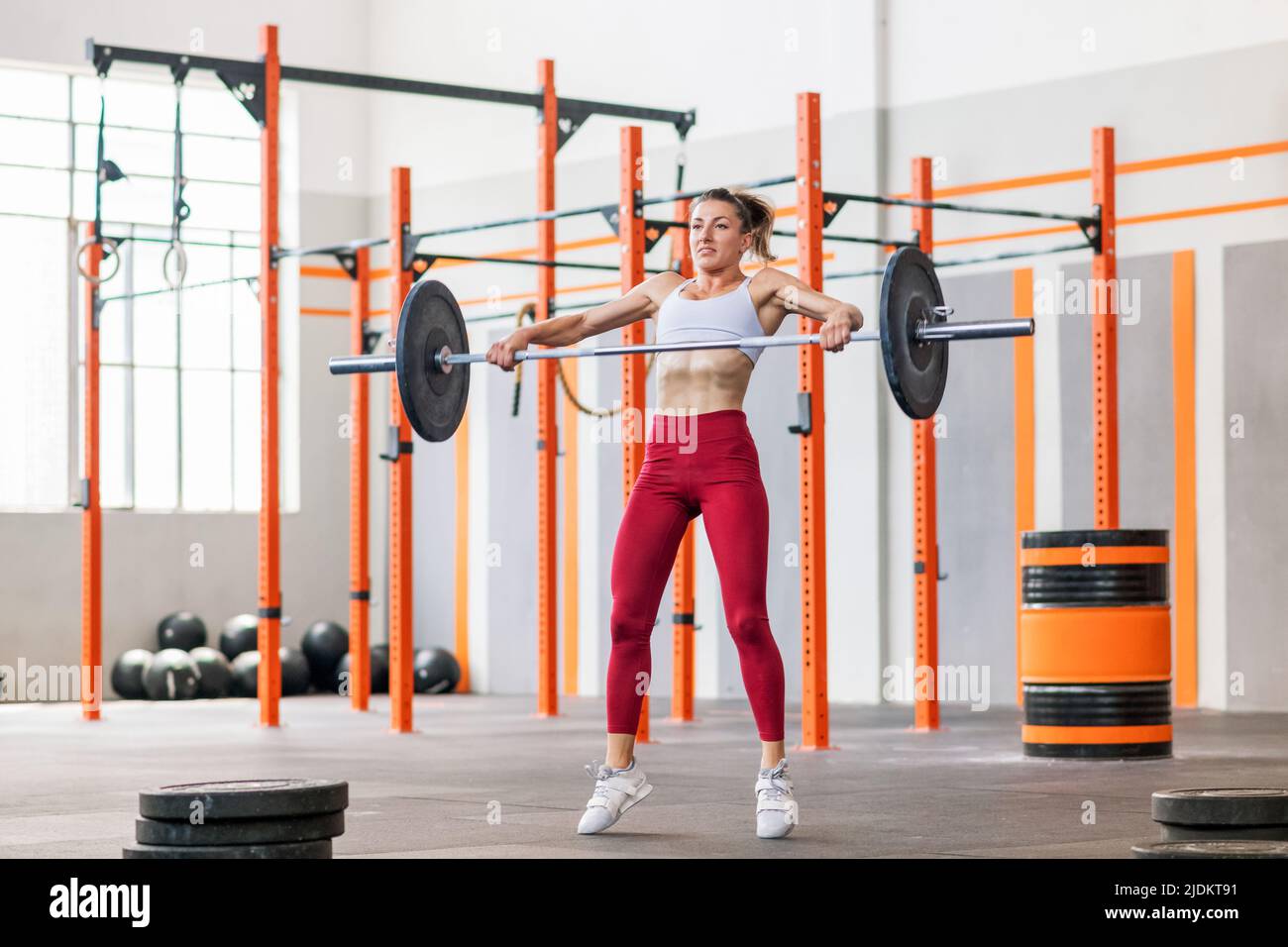 Posez une jeune femme musclée en train d'effectuer un match de barbelette dans une salle de gym en levant les poids à la hauteur des épaules Banque D'Images