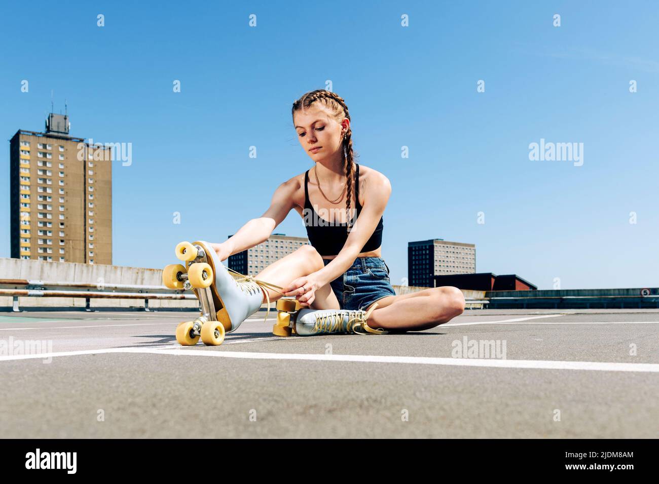 Jeune fille qui a noué ses patins à roulettes, fond urbain Banque D'Images