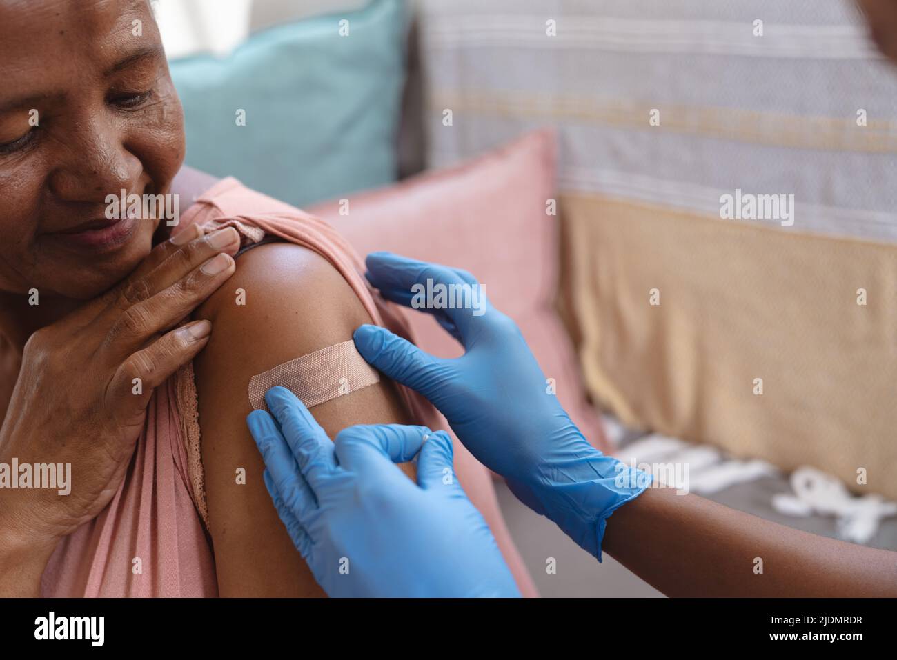 Mains d'un médecin afro-américain portant des gants collant bandage adhésif sur l'épaule d'une femme âgée Banque D'Images