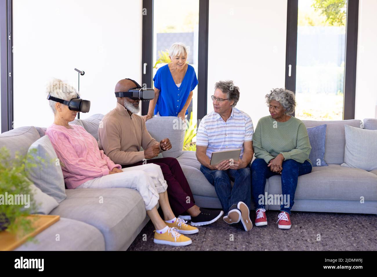 Aînés multiraciaux avec pc numérique regardant des amis en utilisant le simulateur de réalité virtuelle sur le canapé Banque D'Images