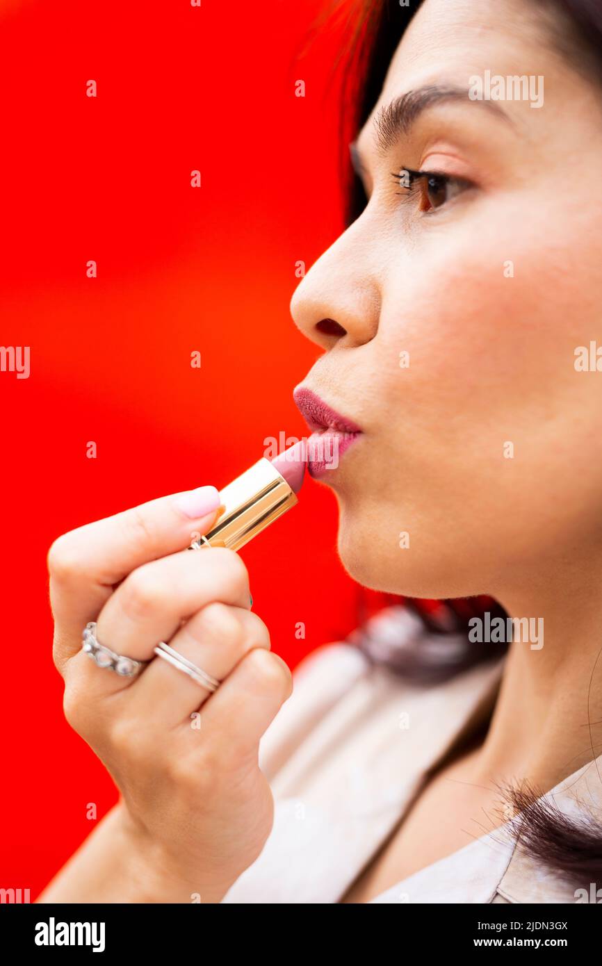 Jeune femme brune utilisant un rouge à lèvres et sur fond rouge Banque D'Images Jeune femme brune utilisant un rouge à lèvres et sur fond rouge Banque D'Images