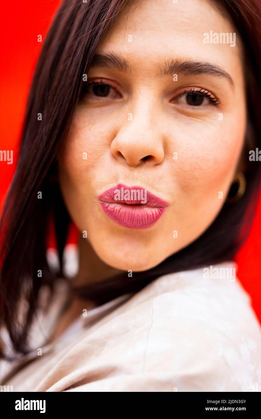 Portrait d'une jeune femme brune envoyant un baiser à l'appareil photo, sur fond rouge Banque D'Images