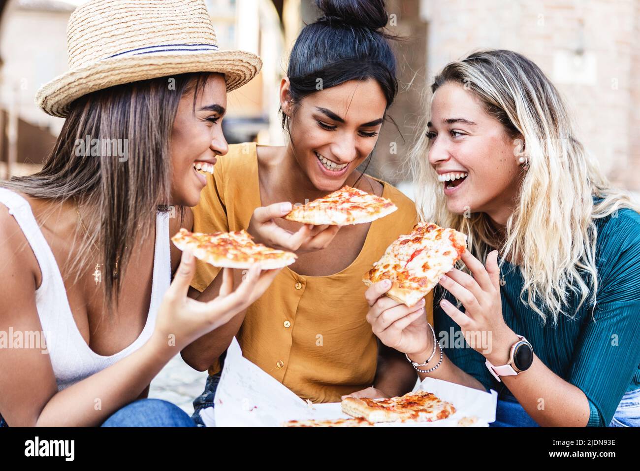 Trois amies multiraciales qui mangent de la pizza italienne pendant les vacances d'été Banque D'Images