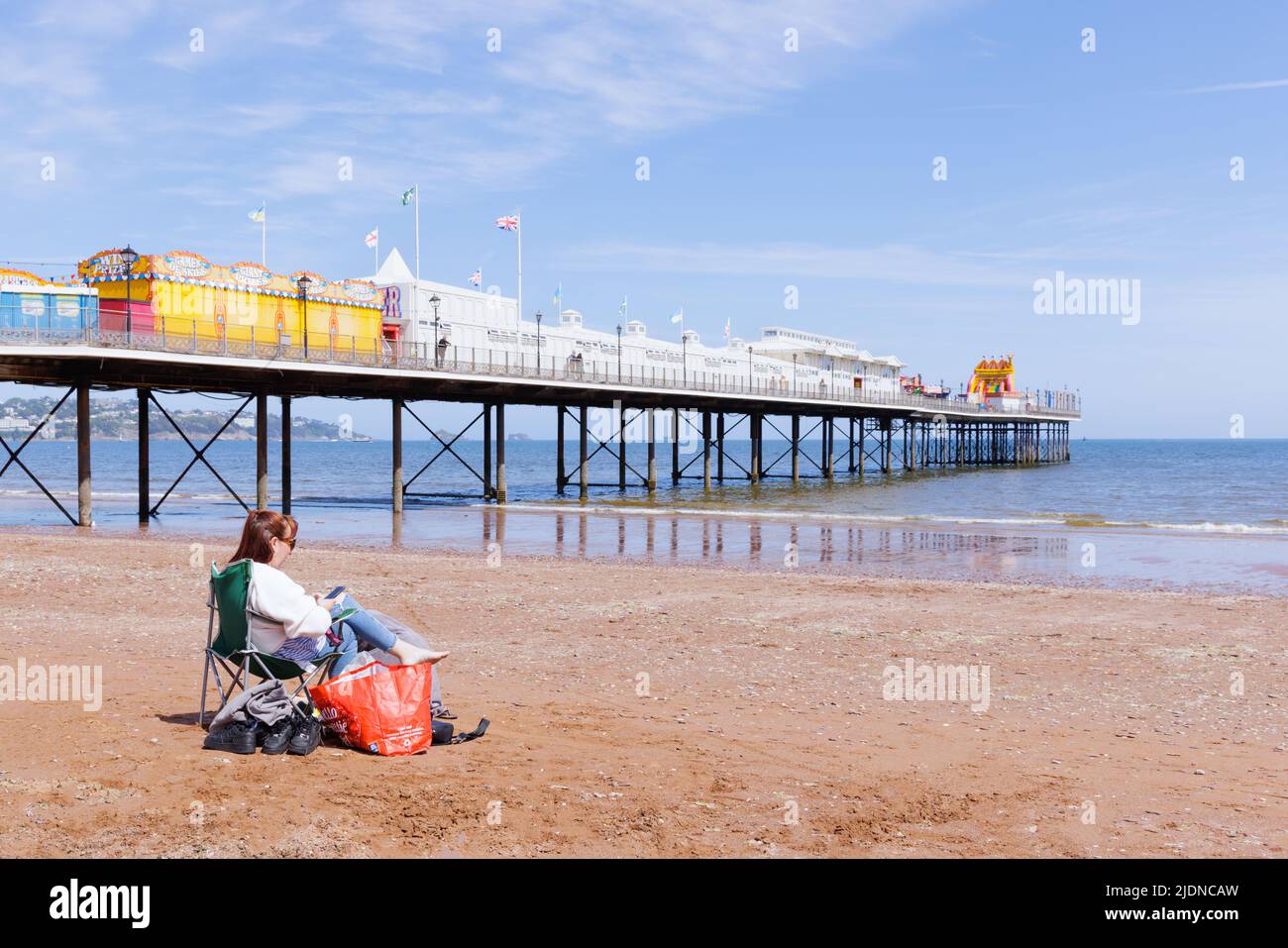 Paignton, Devon, Royaume-Uni, 14 mai 2022 : une femme seule regarde un téléphone mobile tout en étant assise dans un transat sur la plage de Paignton, près de la jetée. Banque D'Images