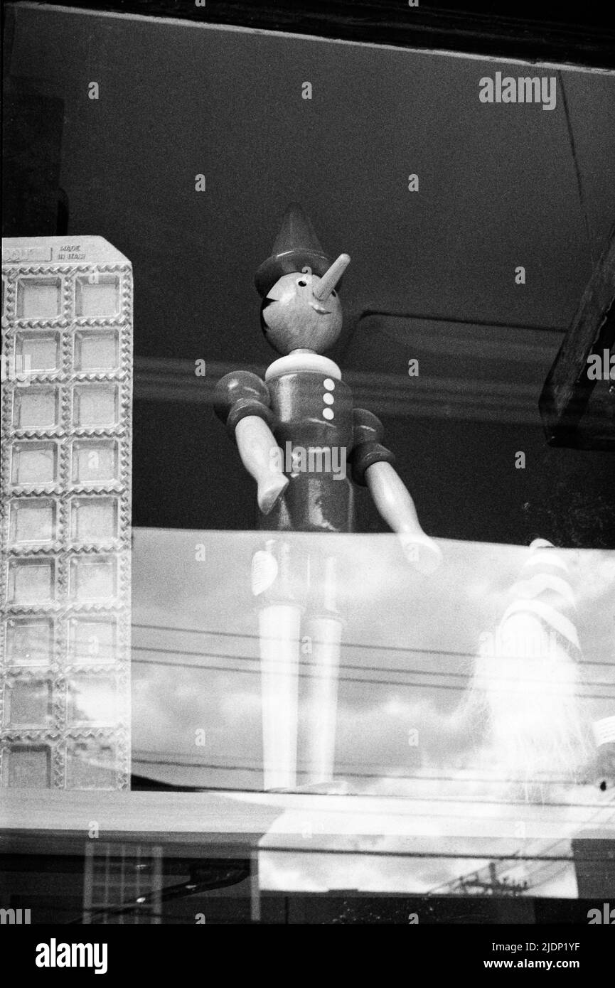 Un jouet en bois Pinocchio debout dans une fenêtre de la façade. Image capturée sur film noir et blanc analogique. Exeter, New Hampshire, États-Unis. Banque D'Images