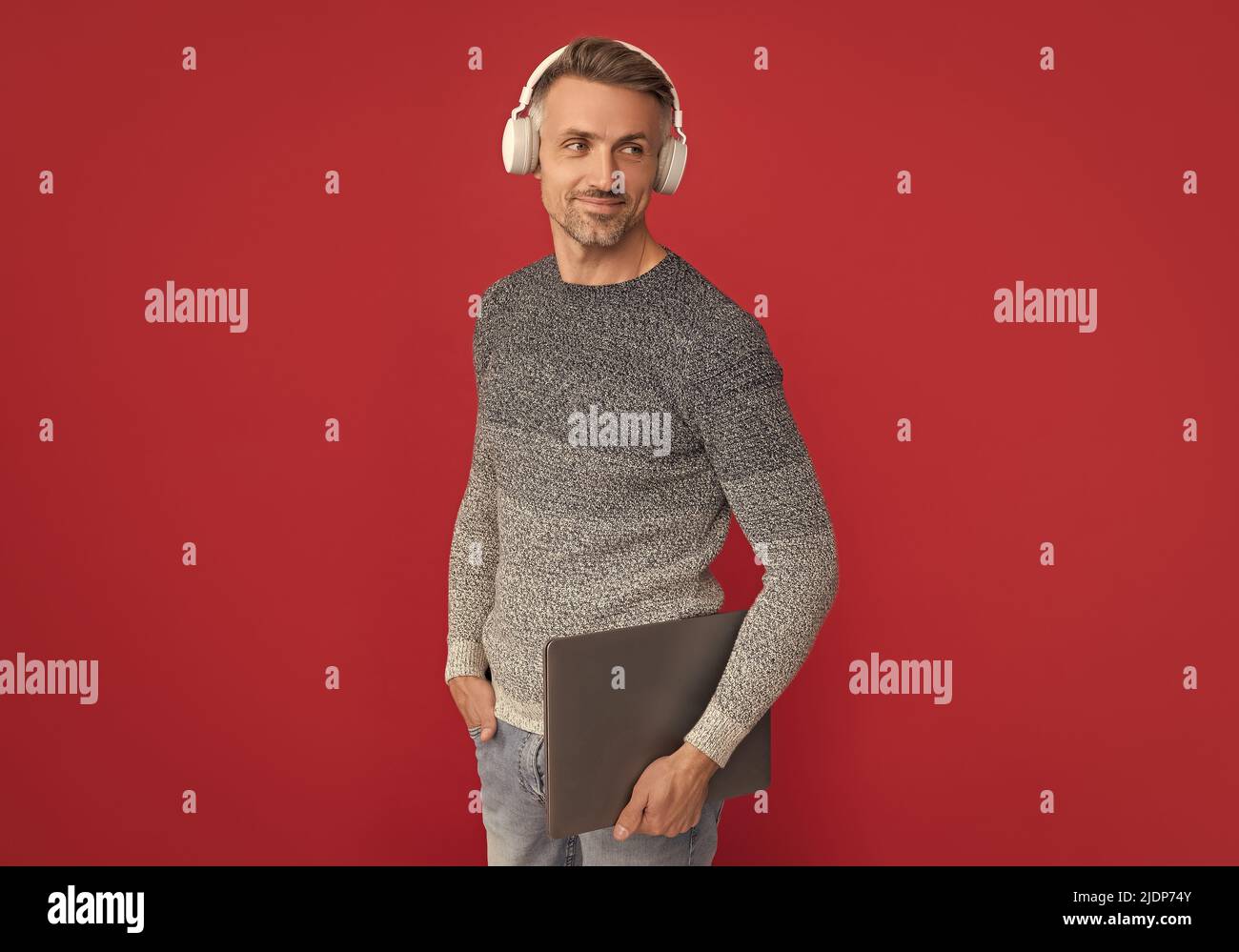 Happy Guy in Wear écouteurs pour écouter le podcast audio sur fond rouge d'ordinateur portable, en ligne Banque D'Images