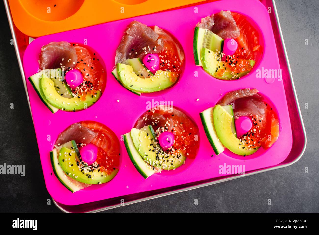 Fabrication de sushi en forme de Donut dans un moule en silicone : ajout de poisson frais, de saumon, de concombre et d'avocat à des moules de beignets Banque D'Images