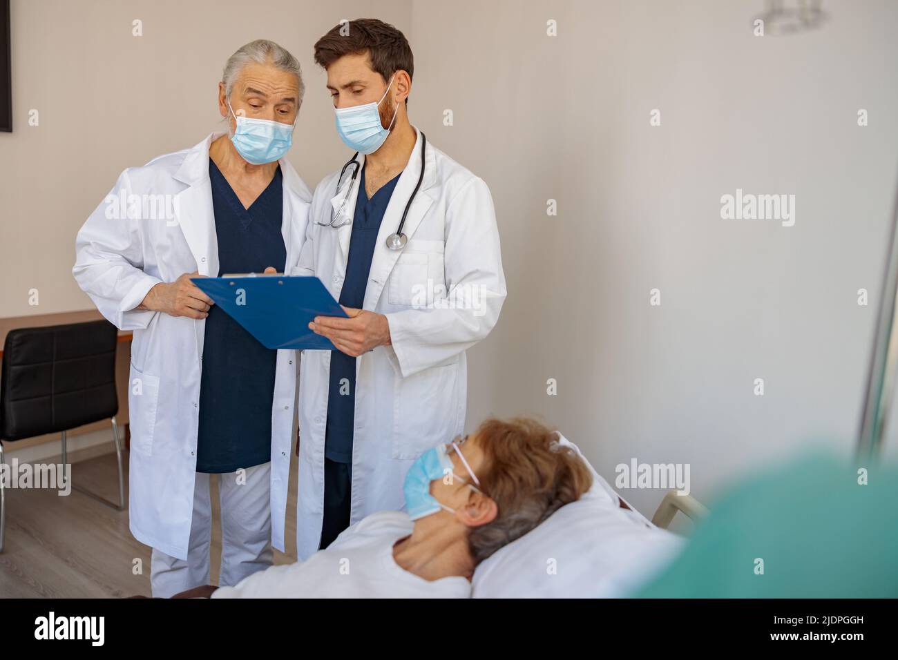 Les médecins professionnels en masque discutent du diagnostic du patient en service hospitalier Banque D'Images