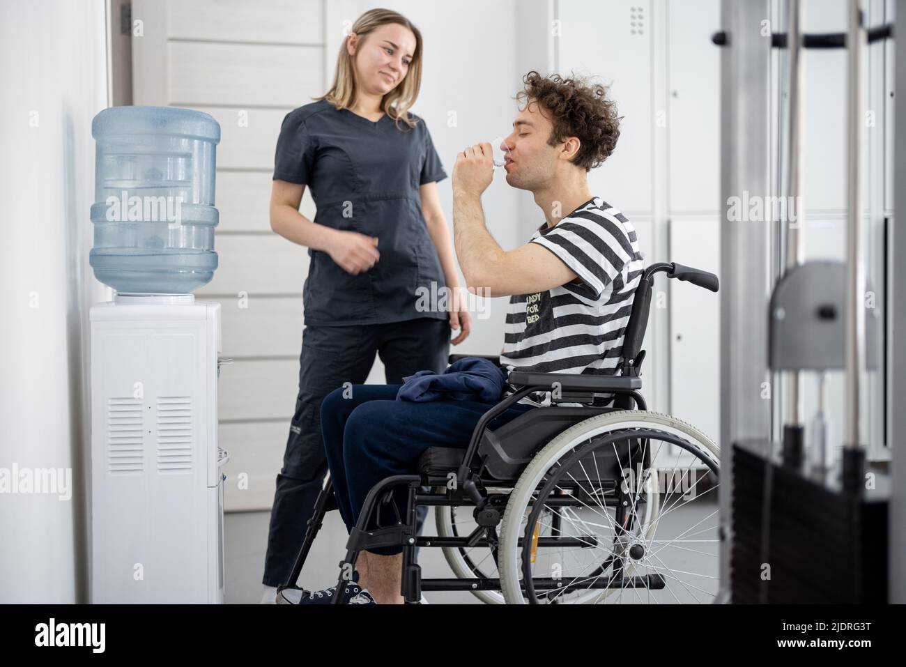 Infirmière aidant un gars en fauteuil roulant à remplir l'eau de la glacière au centre de réadaptation. Banque D'Images