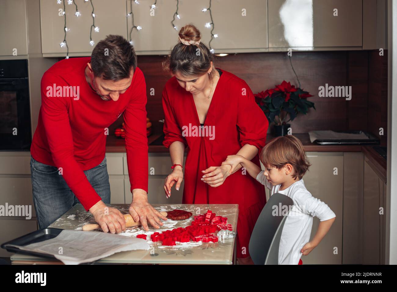 Bonne soirée en famille. Veille de Noël pour les jeunes familles en vêtements rouges, père, mère et enfant. Fils, garçon, biscuits de cuisson de 4 ans. Banque D'Images