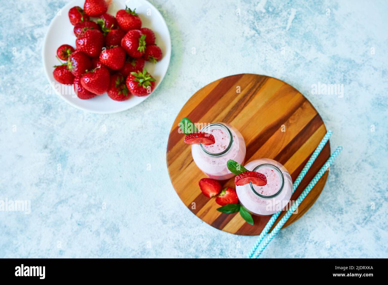 Smoothie aux fraises ou milkshake dans un pot en verre avec baies sur fond de béton bleu. Banque D'Images