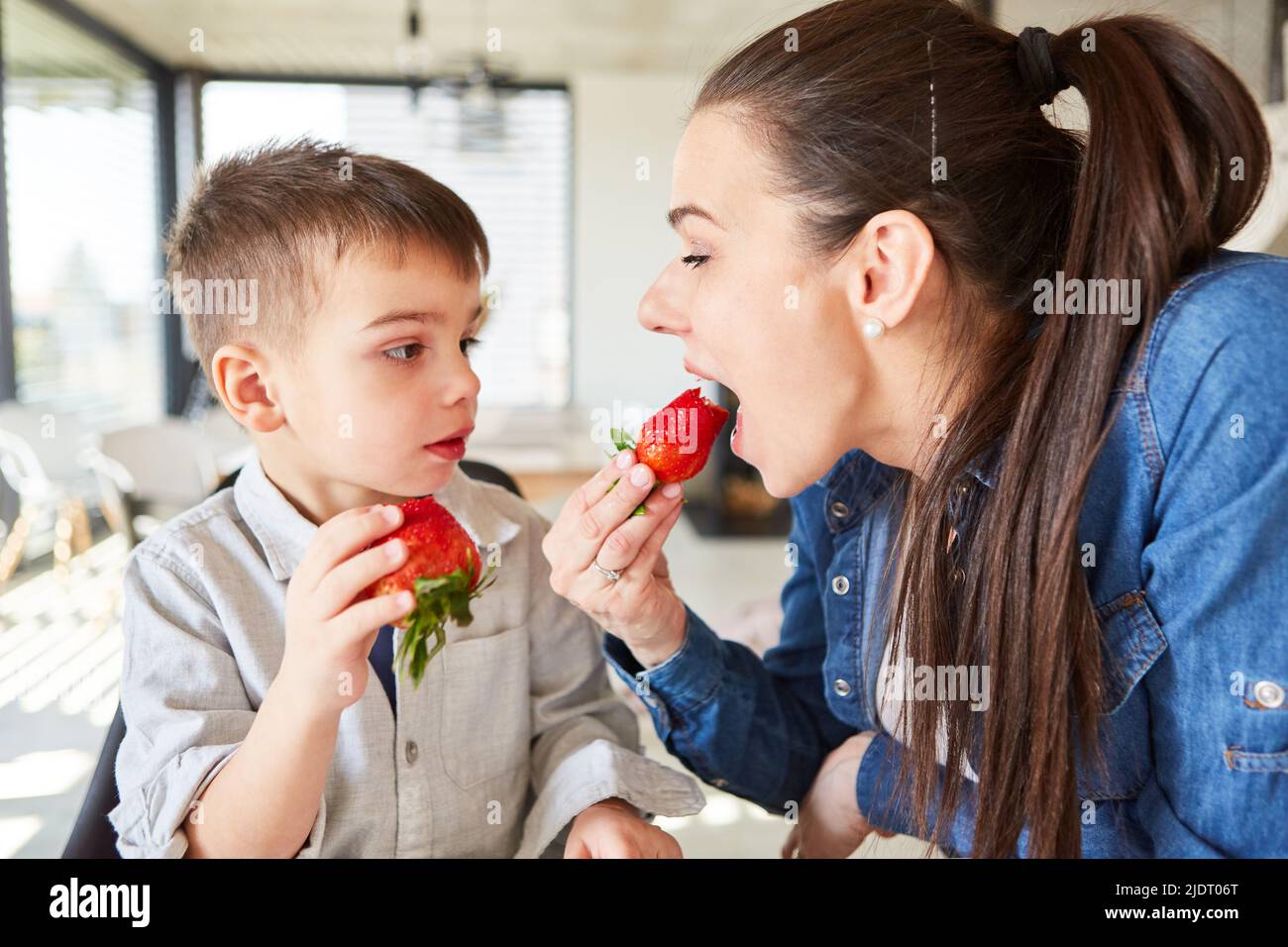 Mère piquant dans une fraise fraîche tout en grignotant avec son petit fils dans le salon Banque D'Images