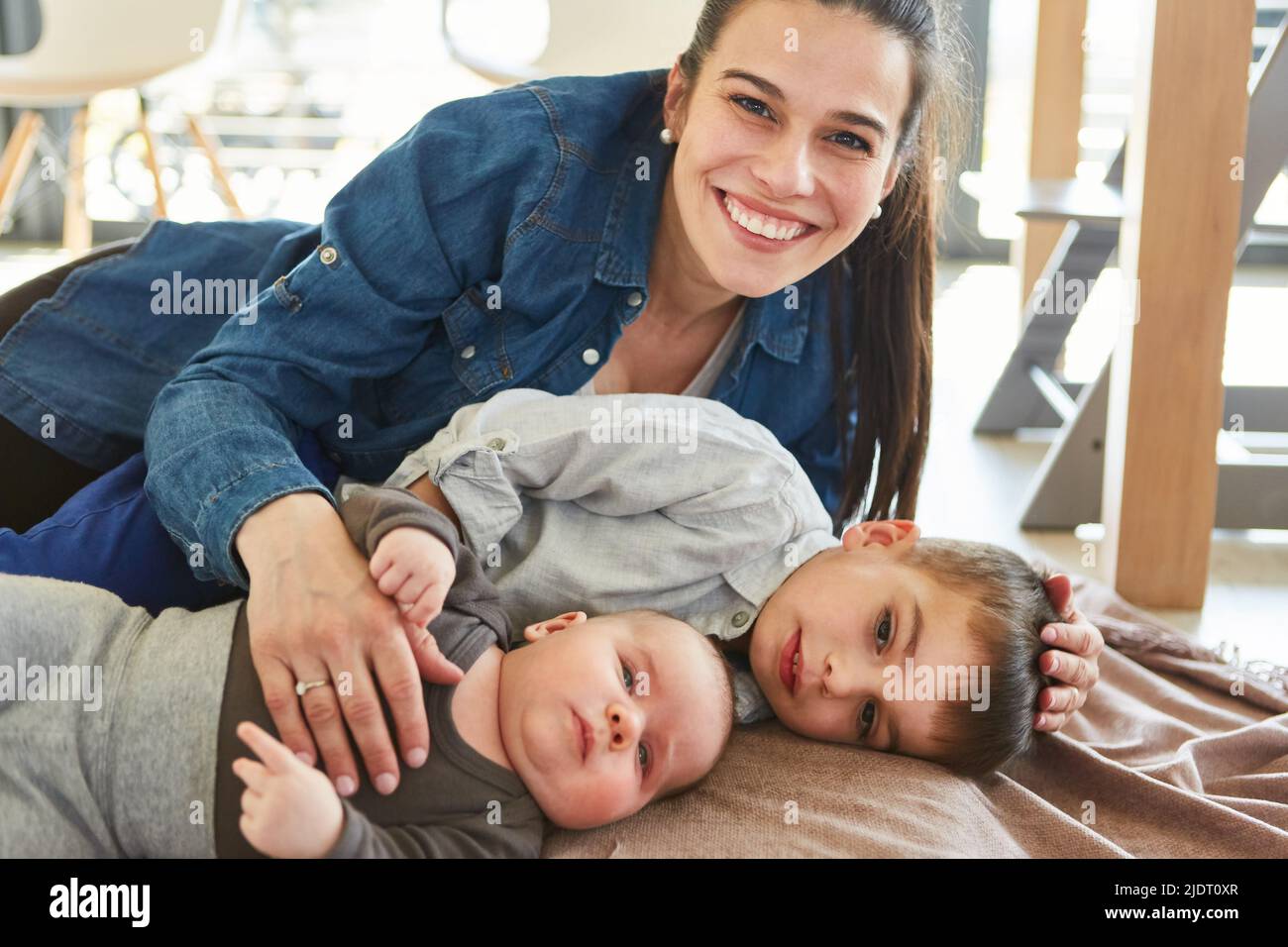 Une seule mère heureuse qui se câlin avec bébé et enfant dans le salon à la maison Banque D'Images