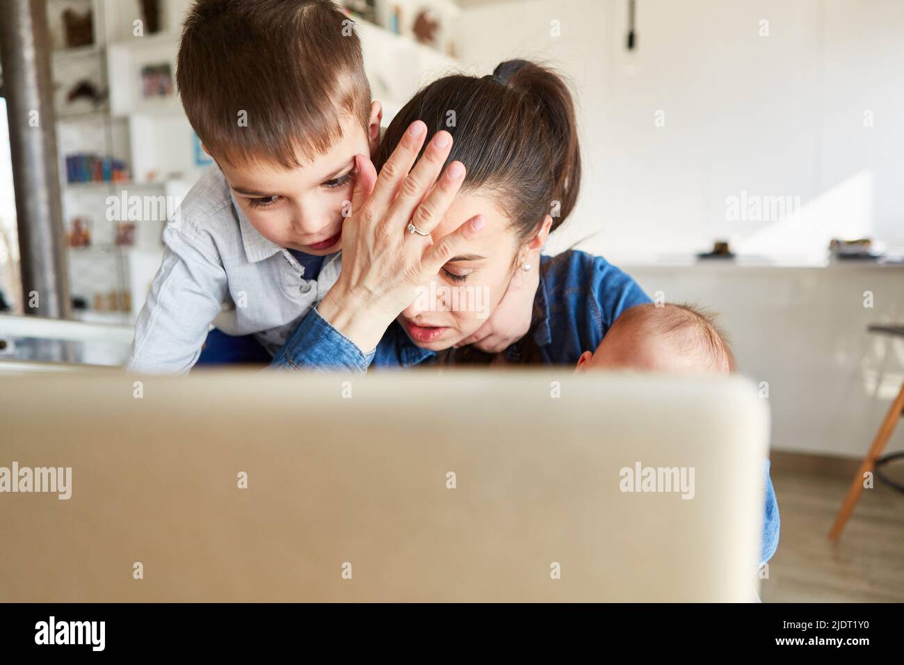 Une mère célibataire avec un brunissage est assise à l'ordinateur dans le bureau à la maison avec son bébé et son enfant Banque D'Images