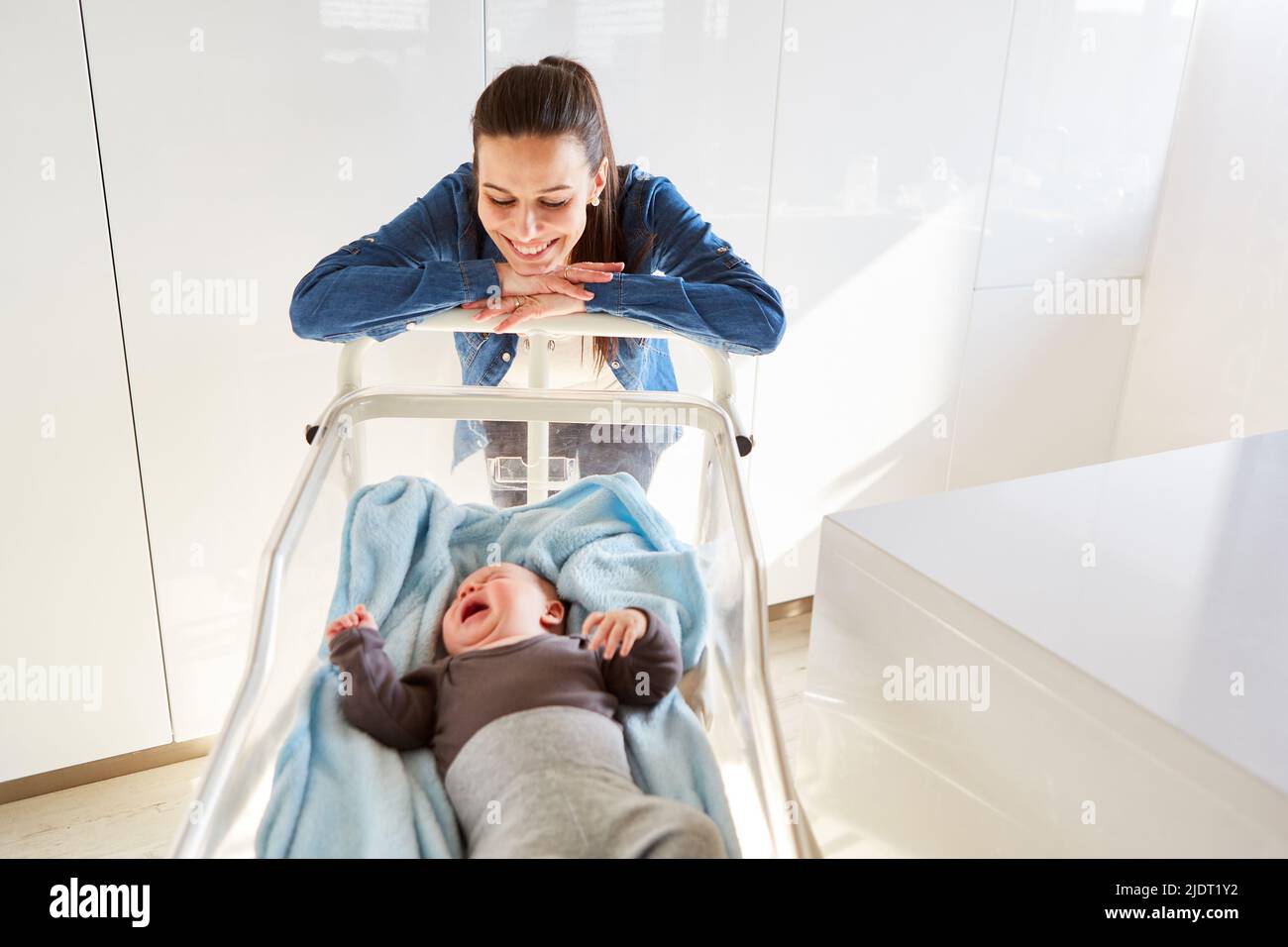 Une mère heureuse regarde fièrement et avec amour son bébé qui pleure dans le lit bébé Banque D'Images