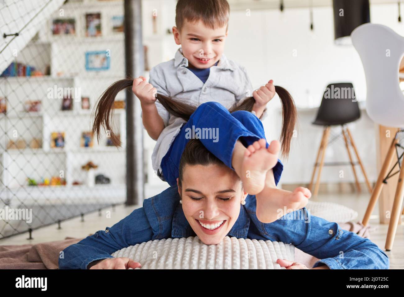 Le petit garçon se joue dans la salle de séjour et tire les cheveux longs de sa mère Photo Stock