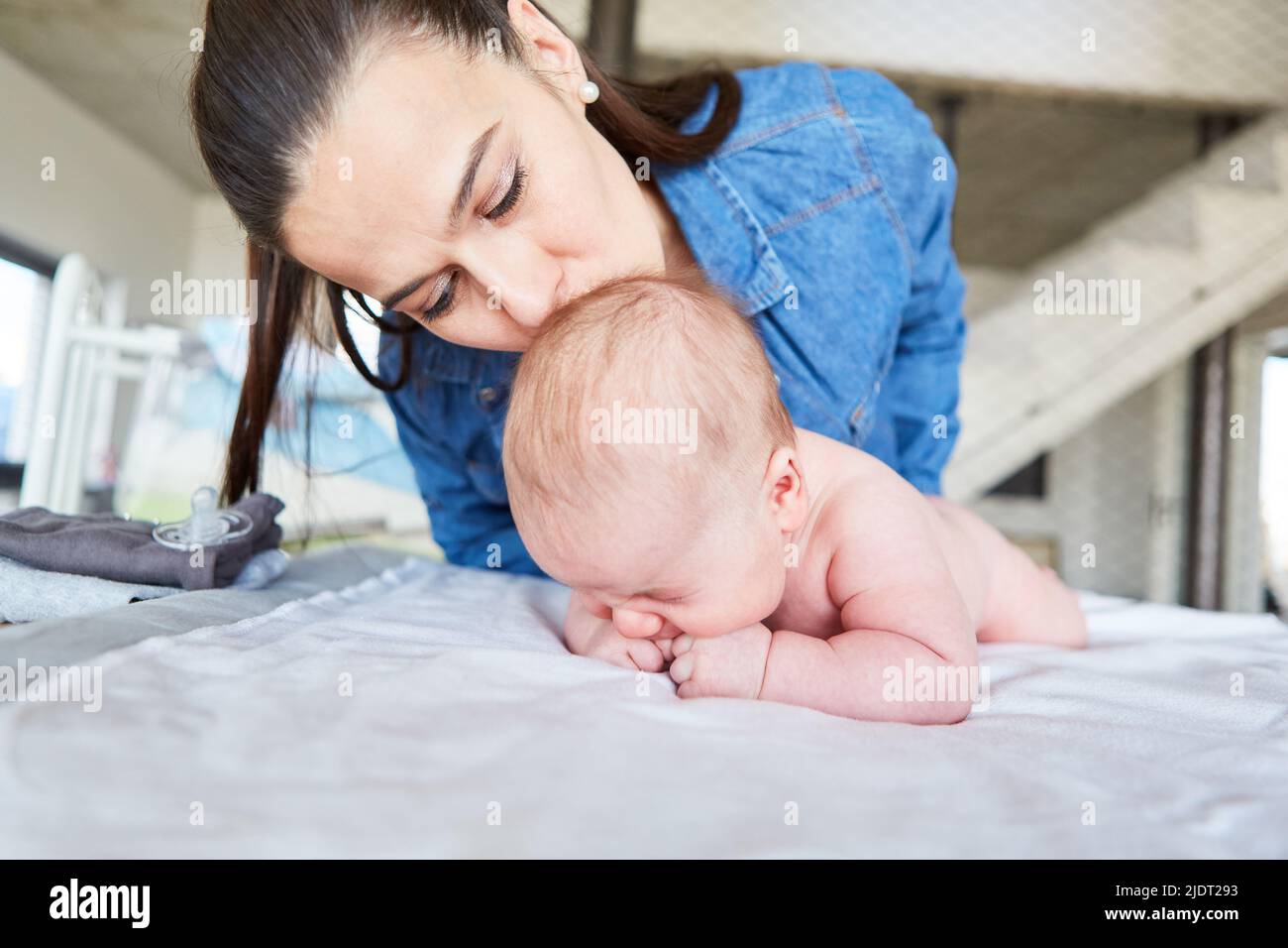 Mère donne à son nouveau-né un baiser tendre tout en changeant la couche Banque D'Images