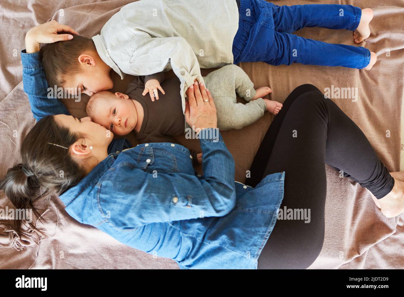 Bébé reçoit un baiser de la mère et du frère tout en se câlinant sur une couverture dans le salon Banque D'Images
