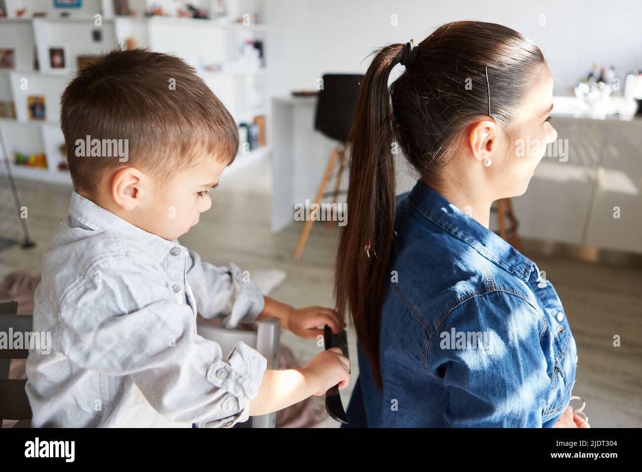 Petit garçon peignant les cheveux longs de sa mère comme un jeu à la maison dans le salon Banque D'Images