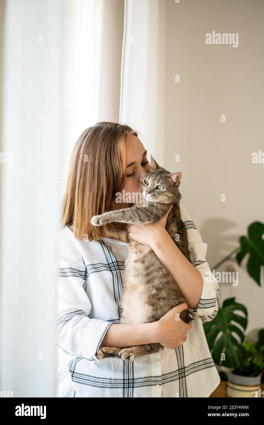 Photo intérieure d'une femme incroyable tenant un animal de compagnie. Portrait d'une jeune femme tenant un chat rayé mignon avec des yeux verts. Femme embrassant son adorable chaton. Adorable concept d'animal domestique. Photo intérieure d'une femme incroyable tenant un animal de compagnie. Banque D'Images