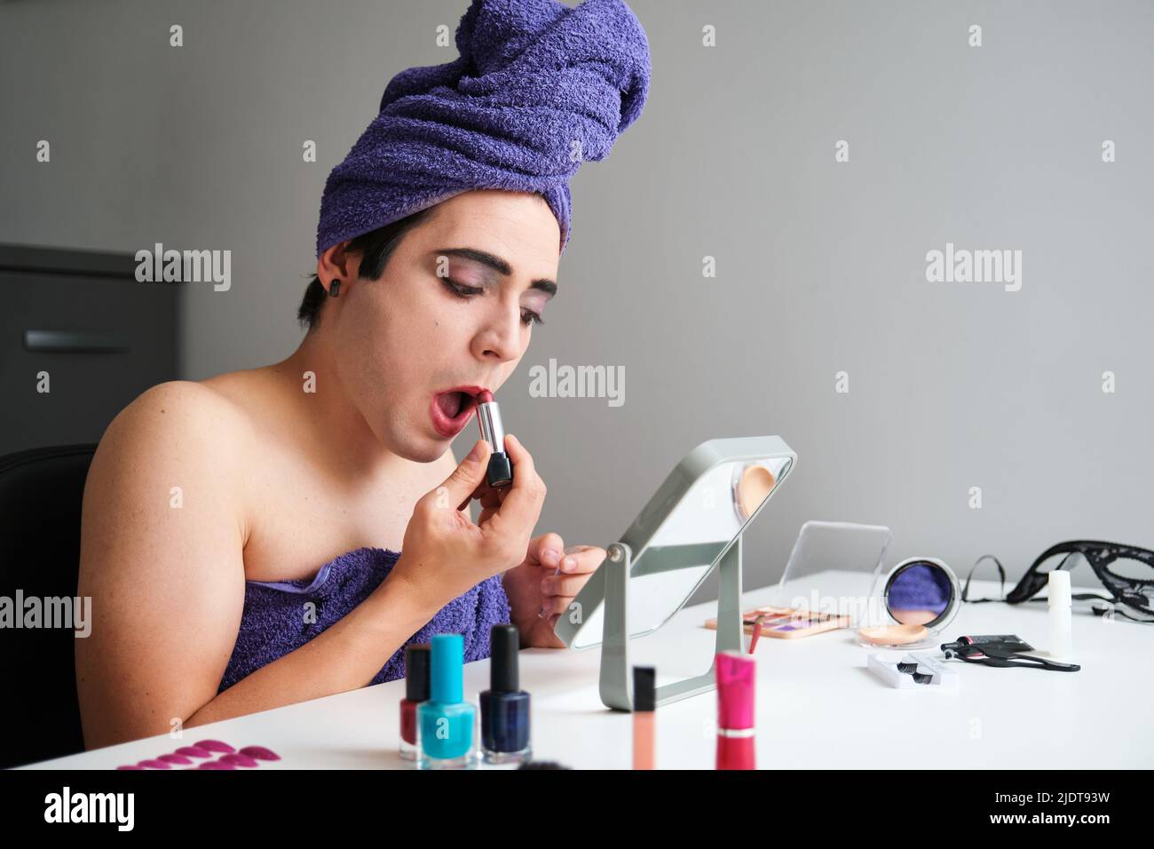 Jeune homme transgenre appliquant le rouge à lèvres. Banque D'Images
